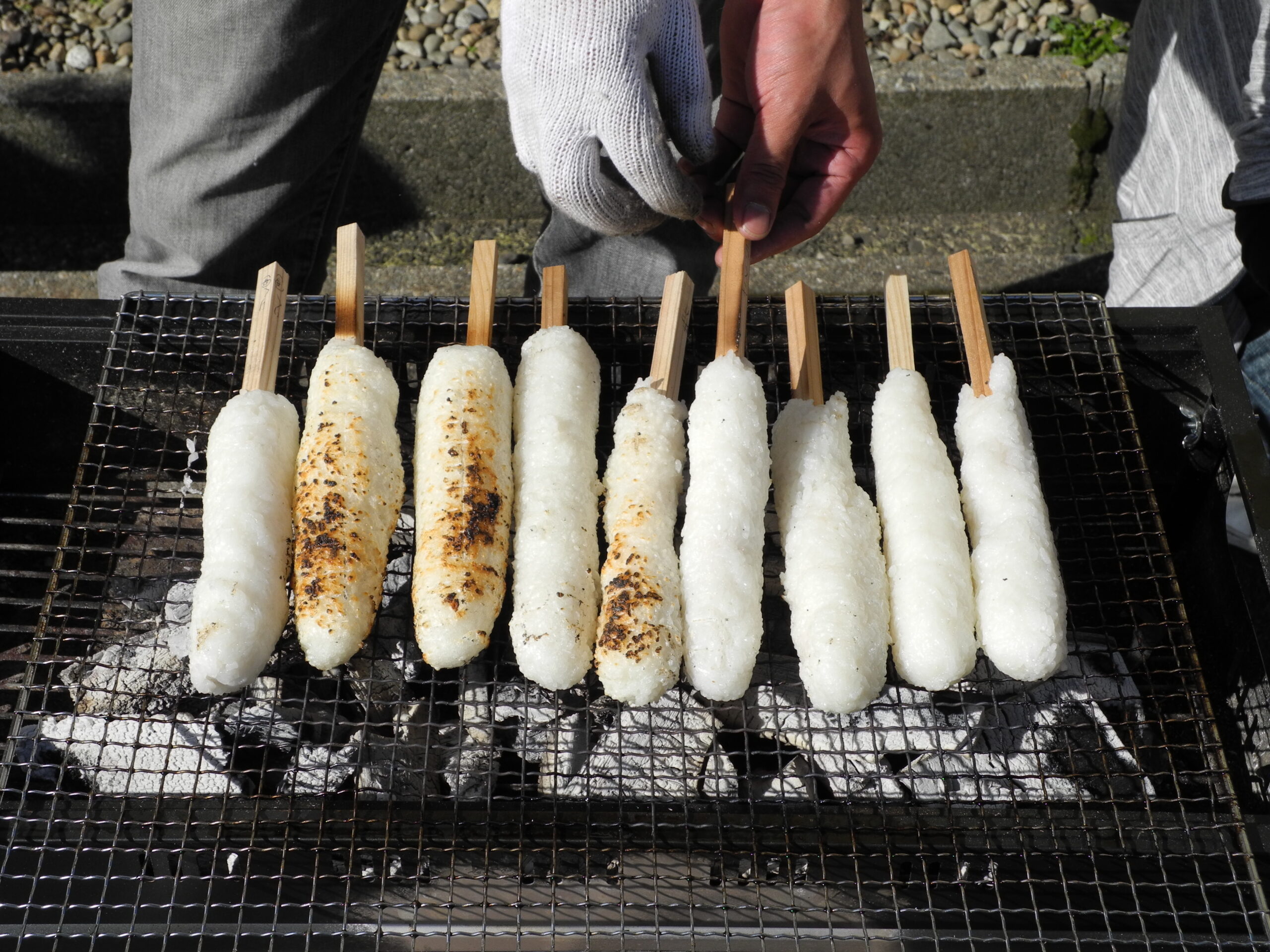 Kiritanpo being grilled over an open flame, developing a golden exterior