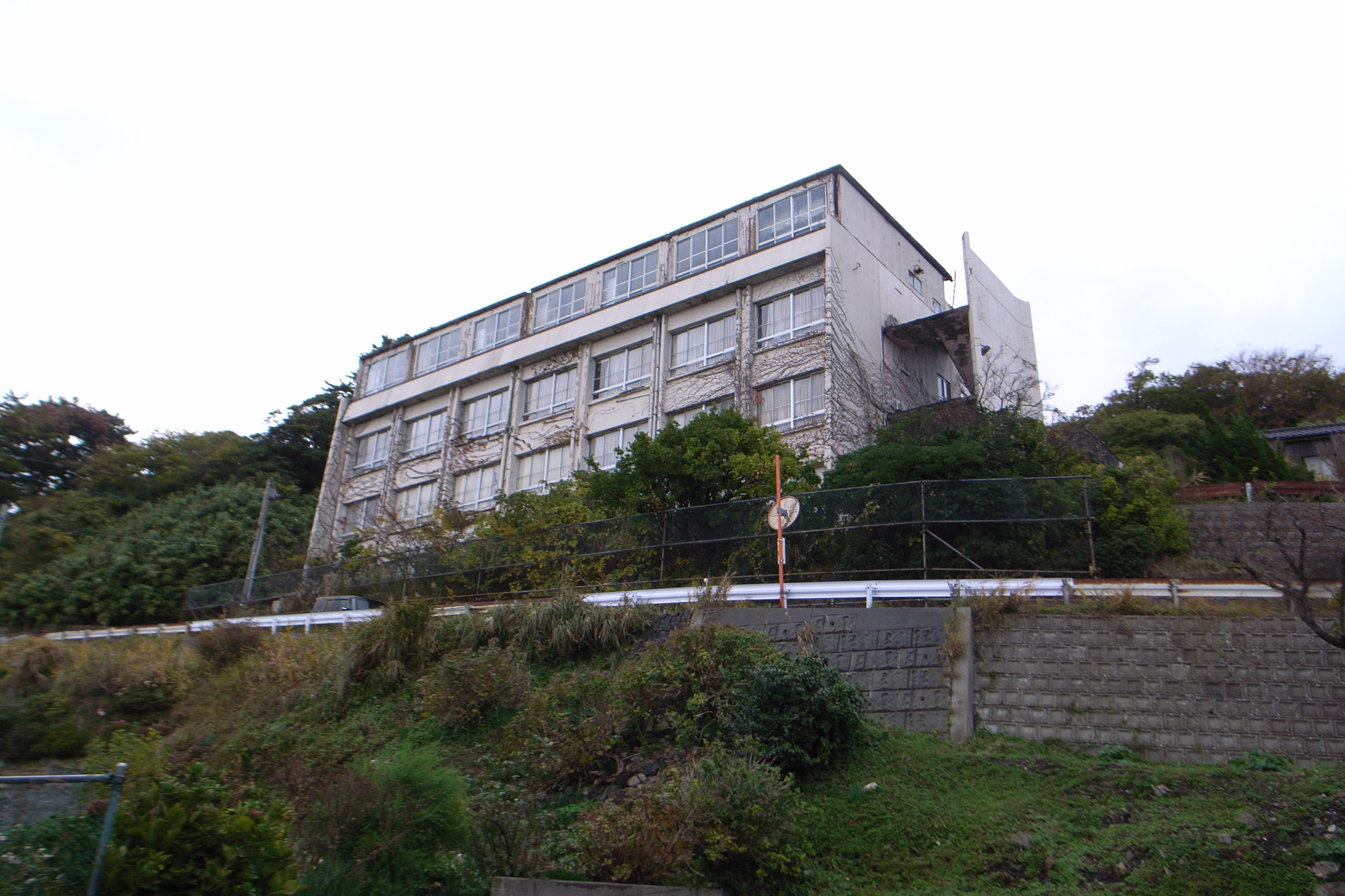 Exterior of abandoned hotel building with overgrown vegetation, structural decay visible