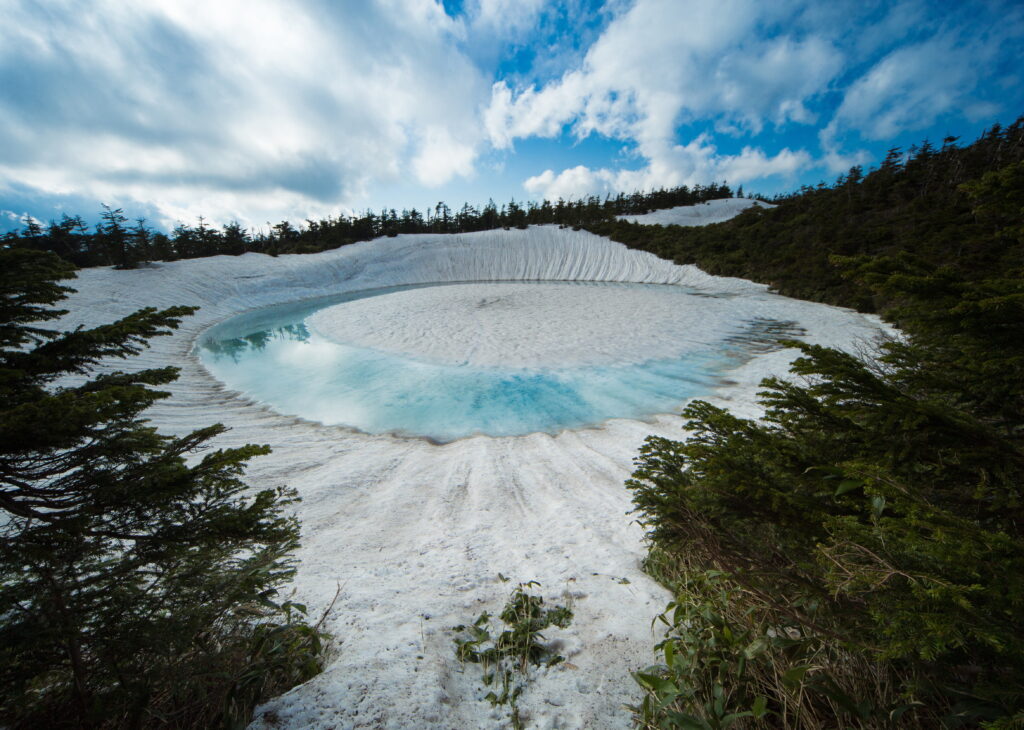 Hachimantai Dragon Eye lake seen from above, a circular crater lake with a stunning iris-like pattern of ice and water