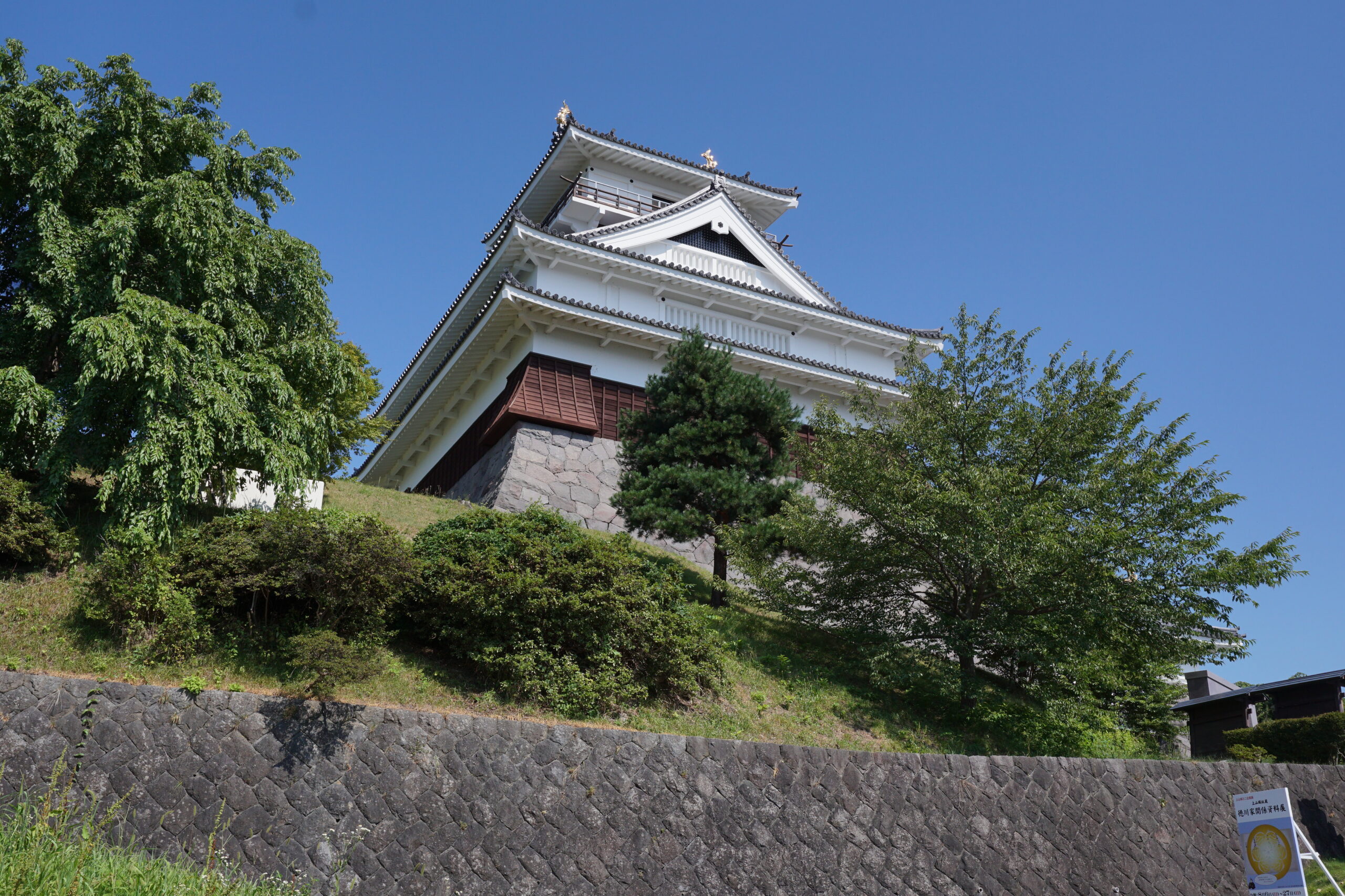 Kaminoyama Castle in summer with lush green grounds and the castle tower reflected