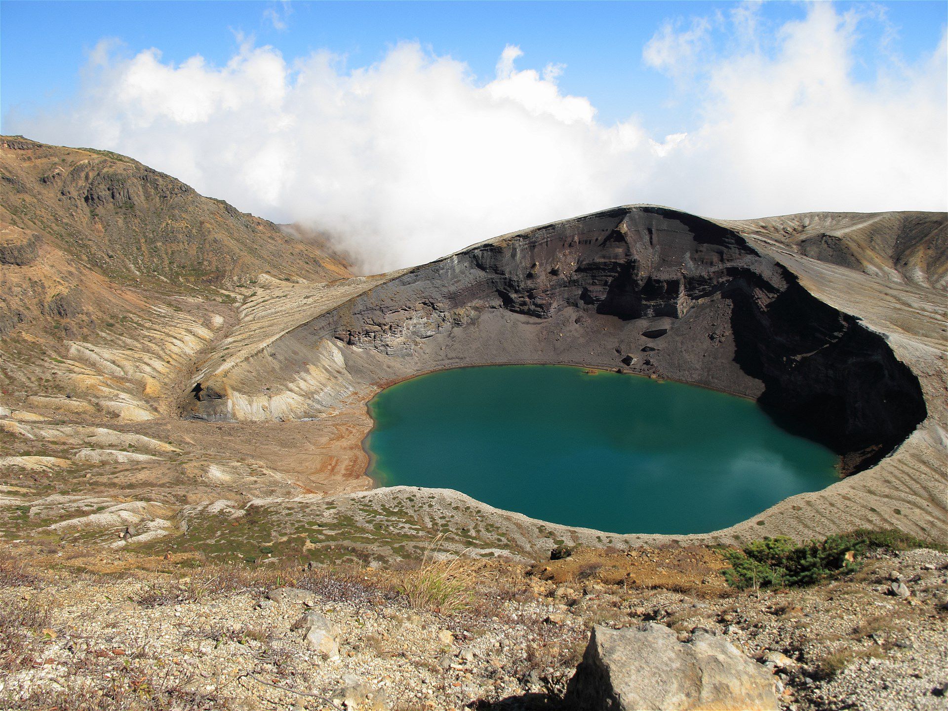 Aerial-style view of Zao Okama crater lake showing the circular volcanic crater and surrounding mountain terrain