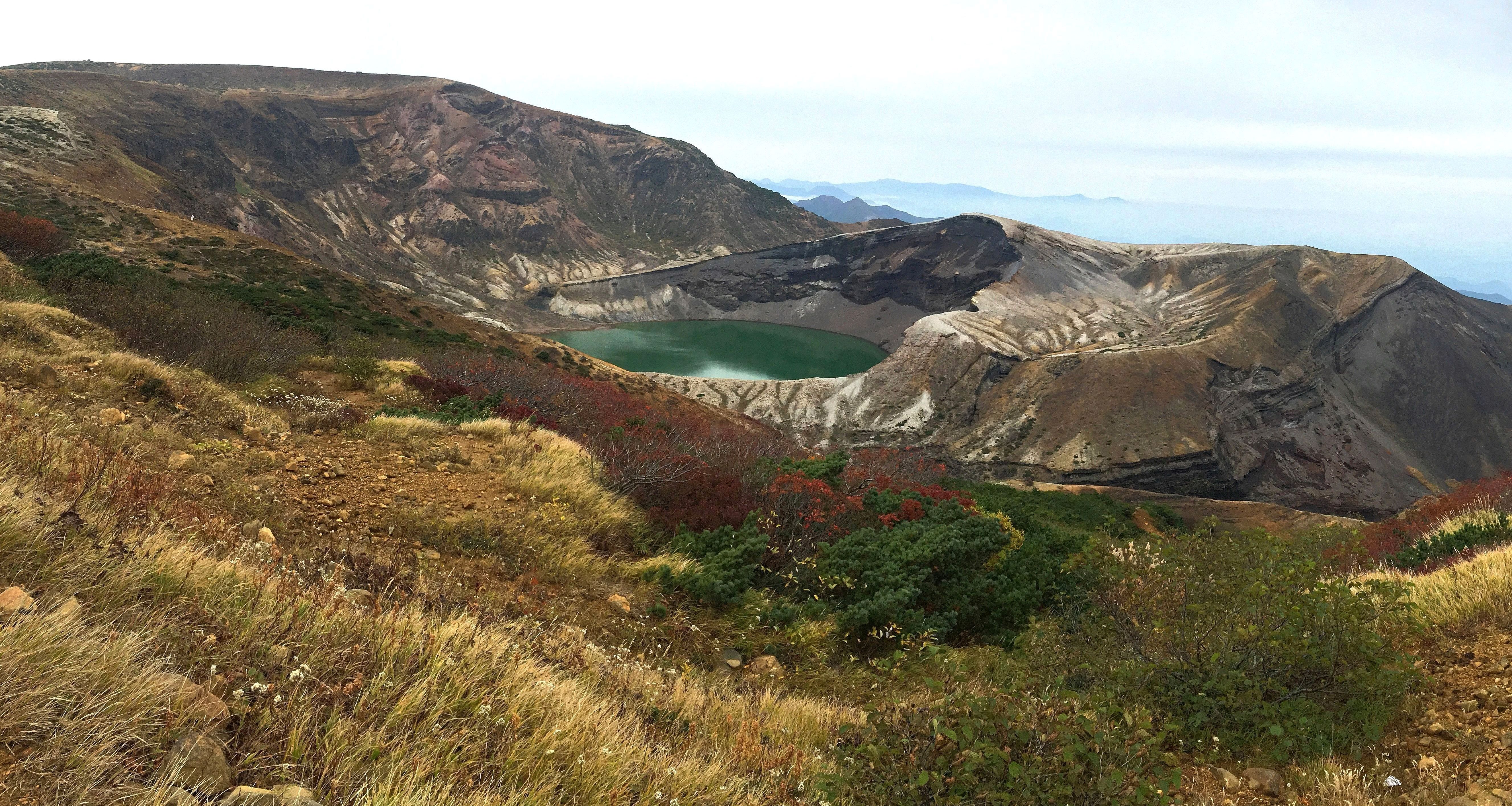 Zao Okama crater lake with vivid green-emerald water surrounded by volcanic rock and autumn foliage