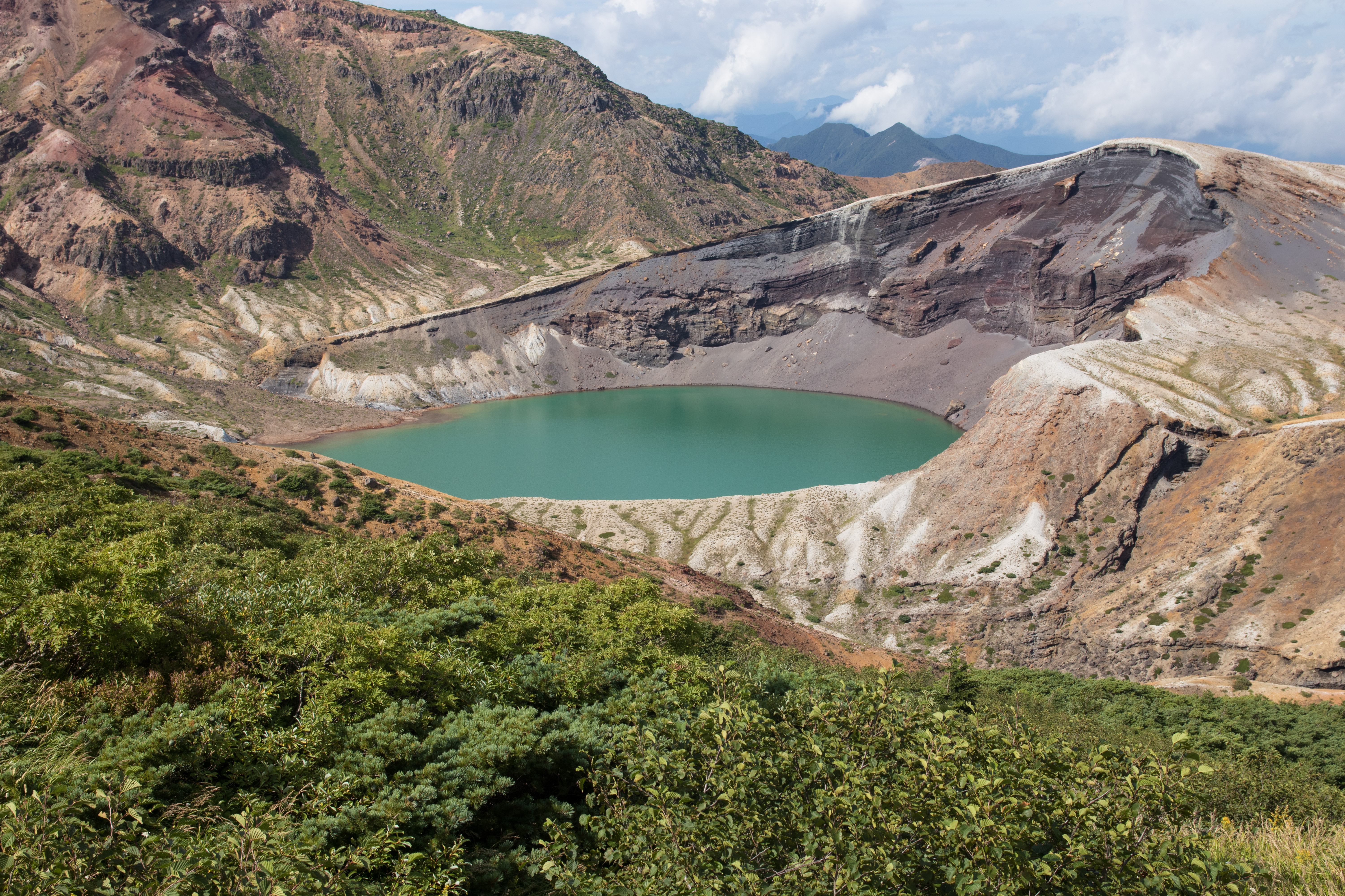 Side view of Zao Okama crater lake showing the volcanic rim and colored water from multiple angles