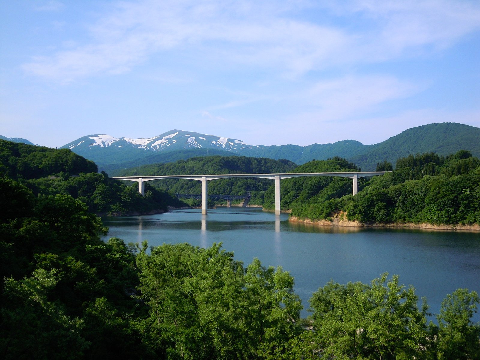 Mount Gassan seen from a bridge with its snow-covered flanks reflected in the water below